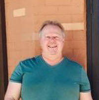 Smiling person in green shirt standing outdoors.