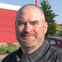 Smiling man outdoors near a red building.