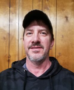 Man wearing cap and hoodie indoors, wooden background.